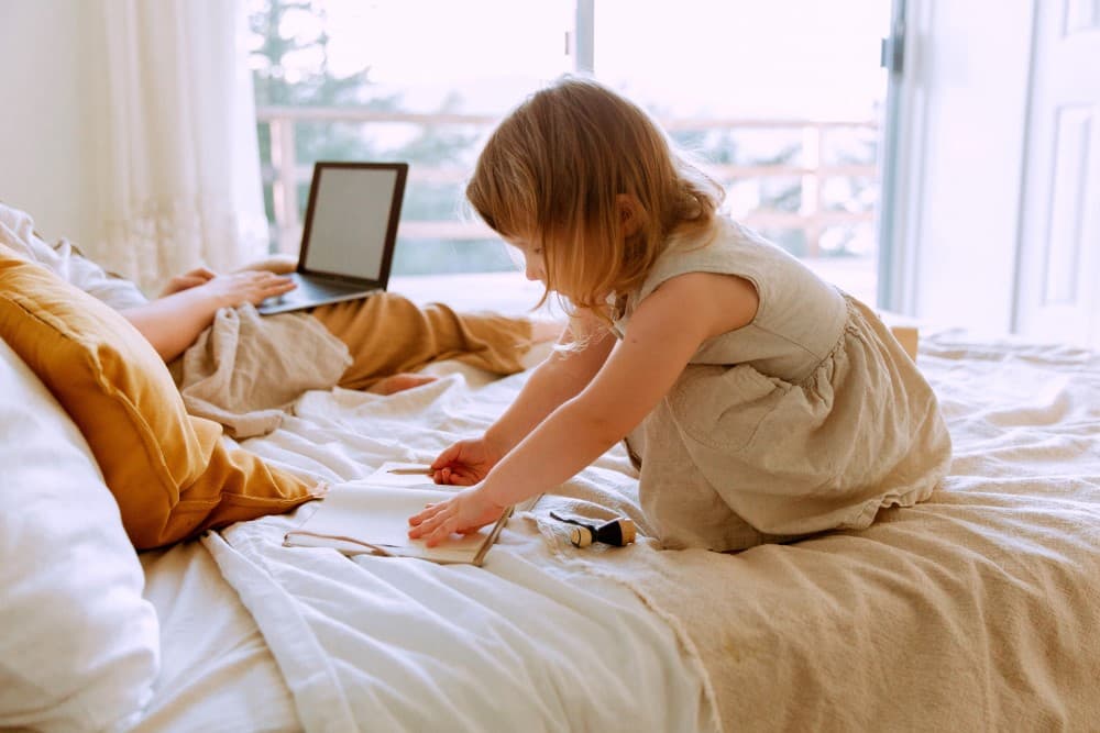 Une mère travaillant sur son lit avec sa fille.